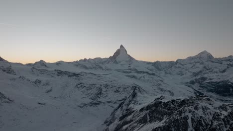 Gebirgsdrohnenantenne-Mit-Atemberaubendem-Blick-Auf-Das-Matterhorn-Zermatt-In-Den-Schweizer-Alpen-Bei-Sonnenuntergang-Im-Winter-Mit-Goldenem,-Klarem-Himmel-Und-Darüber-Fliegendem-Flugzeug