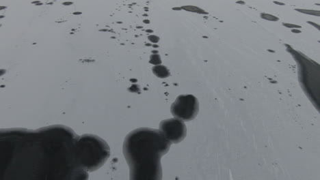Tilt-down,-dark-abstract-spots-on-frozen-lake
