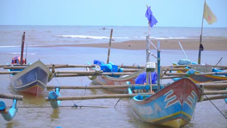 Close-up-shot-of-Indonesian-fisherman-boats-swimming-in-water-at-port-with-ocean-waves-in-background