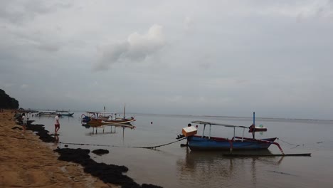 Sanur-Beach-Bali-Indonesia,-Stillness,-Water-Reflected-with-Clouds,-People,-Boats-Docked,-Sea-Buoy-in-Calm-Weather,-Cloudy-Sky,-White-Sand,-Coastline