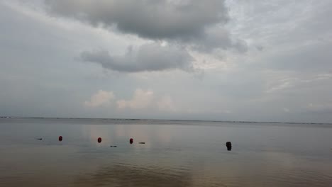 Boya-De-Mar-Flota-En-El-Agua-De-La-Playa-De-Sanur,-Bali,-Indonesia,-Nubes-Reflejadas,-Orilla-Y-Horizonte-Horizonte-Azul-Y-Blanco