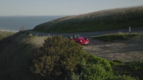 Aerial-drone-shot-reveals-a-red-Porsche-1993-Carrera-S-from-behind-a-bush-overlooking-the-ocean-near-Malibu