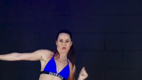 Enthusiastic-female-modern-urban-dancer-performing-against-blue-studio-wall,-Close-up-shot