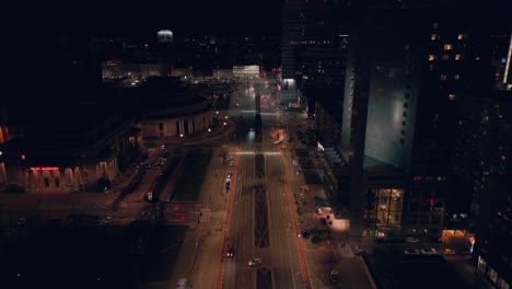 Cars-driving-over-the-wide-road-between-the-high-buildings-at-night