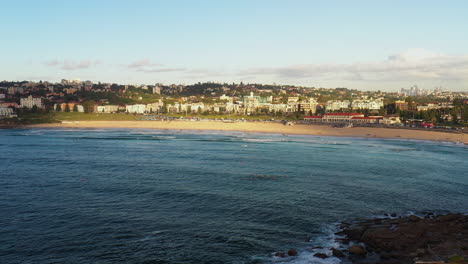 Drone-flying-towards-Bondi-beach-during-golden-hour-in-the-morning,-Sydney-Australia