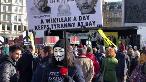 Free-Julian-Assange-Supporter-Wearing-an-Anonymous-Mask-At-Stop-the-War-Protest-in-Trafalgar-Square-London,-walking-through-the-crowd