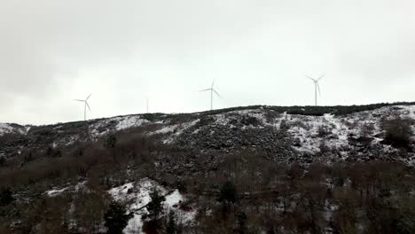 Aerial-shot-over-Snowy-hill-with-3-modern-windmills-on-a-cloudy-day
