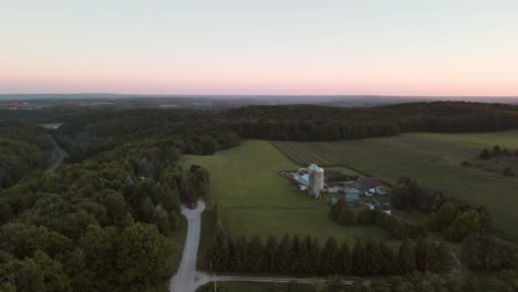 Wide-slow-aerial-orbiting-shot-of-a-farm-with-silos-in-the-rolling-hills-of-northern-Michigan-at-sunset