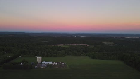 Absteigende-Luftaufnahme-Einer-Farm-Mit-Silos-Und-Scheunen-In-Den-Niedrigen-Hügeln-In-Der-Nähe-Der-Traverse-City-Michigan-Bei-Sonnenuntergang-Mit-Dem-Farbverlauf-Am-Himmel