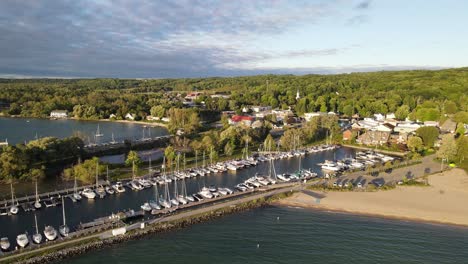 Suttons-Bay-pier-with-moored-sail-boats-and-sandy-beach,-aerial-fly-away-view
