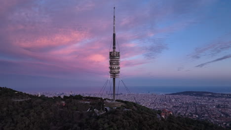 Torre-de-Collserola-communications-tower-at-dusk-on-Tibidabo-with-Barcelona-city-in-background,-Spain