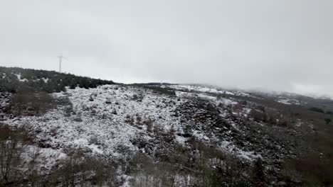 Aerial-shot-of-a-snowy-hill-with-winter-vegetation-and-cloudy-and-foggy-horizon