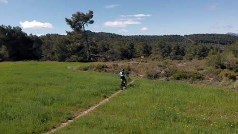 Mountain-biker-rides-through-green-meadow-in-springtime