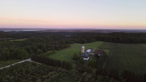 Aerial-flyover-of-a-farm-in-the-wooded-area-and-low-hills-near-Traverse-City-Michigan-at-sunset