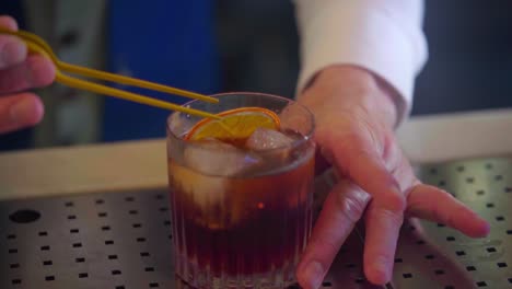 Cocktail-Barkeeper-Bereitet-Einen-Martini-Mit-Einer-Dehydrierten-Orangenscheibe-Und-Eis-Zu