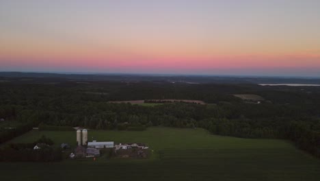 Aerial-dolly-forward-shot-of-a-farm-tucked-into-the-hills-near-Traverse-City-Michigan-during-sunset-with-a-beautiful-gradient-of-color-in-the-sky