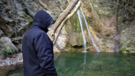Male-hiker-resting-starring-waterfall-small-lake-creek-panning-right-medium-shot