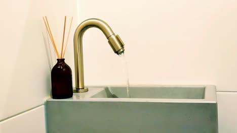 Running-tap-water-out-of-a-golden-toilet-faucet-draining-in-a-concrete-sink