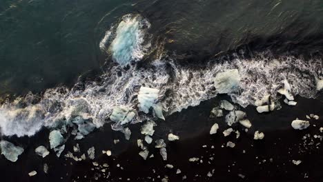 Aerial-top-down-shot-of-waves-reaching-shore-and-beach-with-icebergs-of-Diamond-Beach,-Iceland