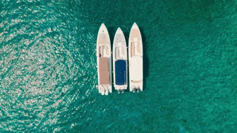 Aerial-top-down-drone-shot-of-three-boats-oark-in-clear-ocean,-Colombia