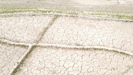Aerial-footage-of-a-dry-pond-reveals-barren-farmland-with-irrigation-channels,-highlighting-the-effects-of-drought