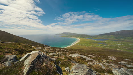 Timelapse-of-seaside-remote-bogland-village-with-sand-beach,-grass-and-rocks-with-clouds-casting-shadows-on-sunny-day-viewed-from-Minaugn-Heights-in-Achill-Island-in-county-Mayo-in-Ireland