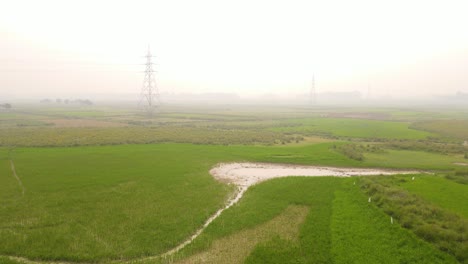 High-voltage-electric-tower-towering-over-a-paddy-foggy-farmland-in-Bangladesh,-creating-a-dramatic-contrast-of-nature-and-technology