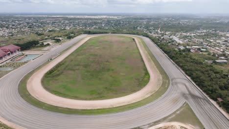 Aerial-top-down-shot-of-empty-horse-racecourse-in-rural-area-with-city-in-background,-Dominican-Republic