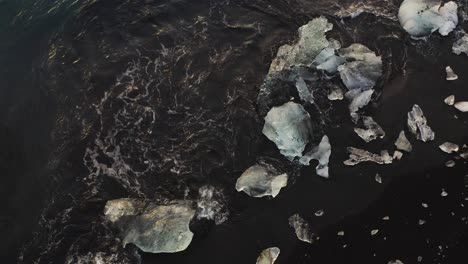 Meereswellen-Krachen-Gegen-Eisige-Eisberge,-Die-Am-Schwarzen-Sandstrand-In-Island-Liegen