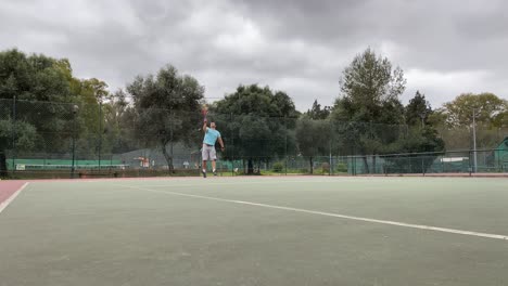 Young-and-athletic-man-doing-serve-and-making-some-smash-to-win-the-point-with-blue-t-shirt-on-cloudy-day-in-Lisbon