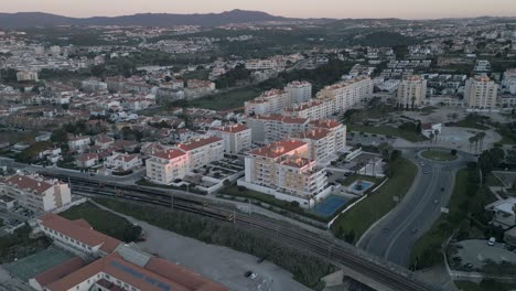 Vista-Aérea-De-Drones-Sobre-Un-Tren-En-Vías-Férreas-Con-Los-Primeros-Rayos-De-Sol-En-Sao-Pedro-Do-Estoril,-Lisboa