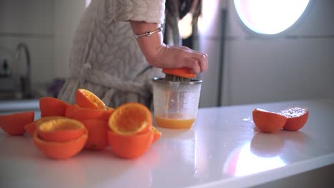 Woman-using-orange-juicer,-squeezer,-reamer-preparing-an-orange-juice-at-home