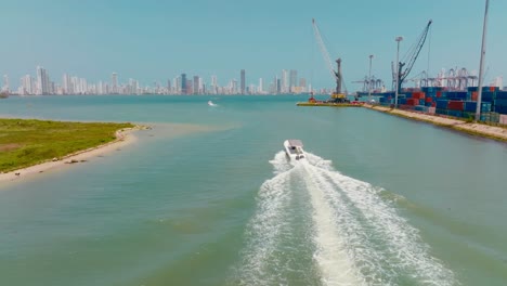 Aerial-Drone-shot-of-boat-passing-the-port-and-in-the-back-there-is-the-city,-Colombia-Cartagena