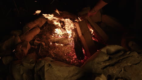 Slow-motion-crackling-campfire-being-tended-to-with-firewood-and-embers-flying-off