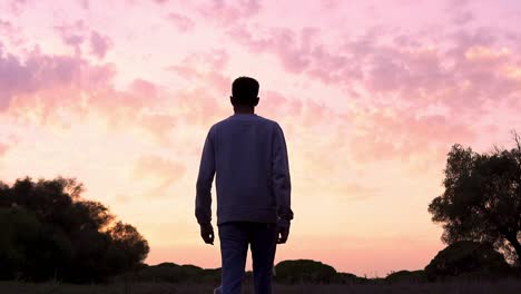 Young-man-walking-forward-in-slow-motion-in-the-countryside-under-an-incredible-pink-sunset
