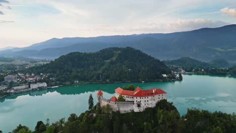Bled-Castle-Overlooking-Peaceful-Lake-Bled-Slovenia,-Aerial-Parallax-Drone-Shot,-Beautiful-Travel-Destination-Early-Morning-Sunrise,-Cinematic-4K