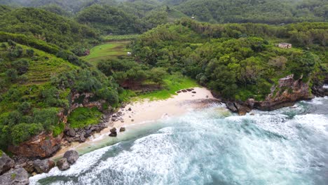 Aerial-top-down-shot-of-ocean-waves-reaching-tropical-private-beach-surrounded-by-deep-rainforest-in-Indonesia