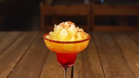 Cocktail-with-pineapple-ice-cream,-chili-powder-and-vodka-on-a-wooden-table,-hand-throws-a-cherry-over-the-cocktail
