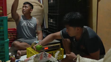 Two-Balinese-men-weigh-and-sort-avocados-into-baskets-in-the-back-of-their-store,-slow-motion