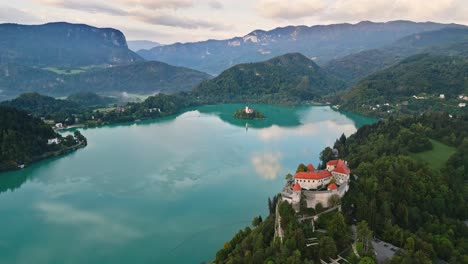 Bled-Castle-On-Rock-Overlooking-Beautiful-Lake-Bled-Slovenia-With-Church-in-Background,-Aerial-Parallax-Drone-Shot,-Early-Morning-Reflection,-Cinematic-4K