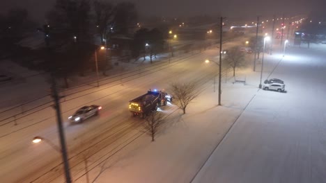 Truck-plow-street-of-Toronto-during-heavy-snowfall,-aerial-drone-follow-view