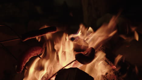 Slow-motion-close-up-of-campfire-with-hot-dogs-being-roasted-on-a-stick