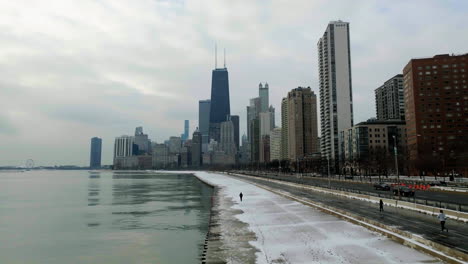 Aerial-view-following-a-person-walking-on-the-Concrete-Beach-towards-skyscrapers-in-Streeterville,-Chicago,-USA