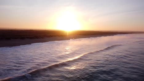 Aerial-flyover-water-of-Atlantic-Ocean-with-small-waves-reaching-supertubos-beach-in-Peniches-at-sunset