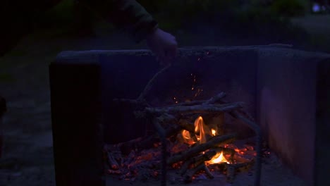Close-up-of-a-person-throwing-sticks-of-wood-into-a-bonfire-in-a-stone-container-in-slow-motion