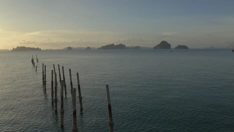 Scenic-aerial-view-of-old-dock-posts-in-the-scenic-Andaman-sea-during-sunset,-following-shot