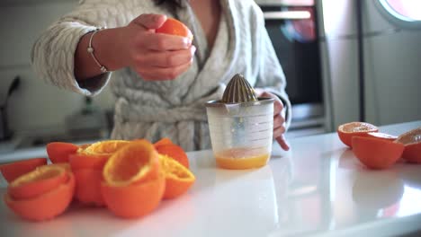 Woman-using-orange-juicer,-squeezer,-reamer-preparing-an-orange-juice-at-home