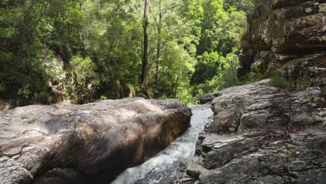 Stream-of-water-carving-channels-through-solid-rock-formation-disappearing-into-a-dense-rainforest-below