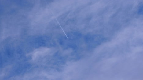 Contrails-and-vapor-trail-lines-from-an-aeroplane-aircraft-flying-overhead-against-a-fine-blue,-slightly-cloudy-sky