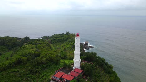 Aerial-view-of-white-lighthouse-on-hill-in-front-of-ocean-in-YOGYAKARTA,-INDONESIA